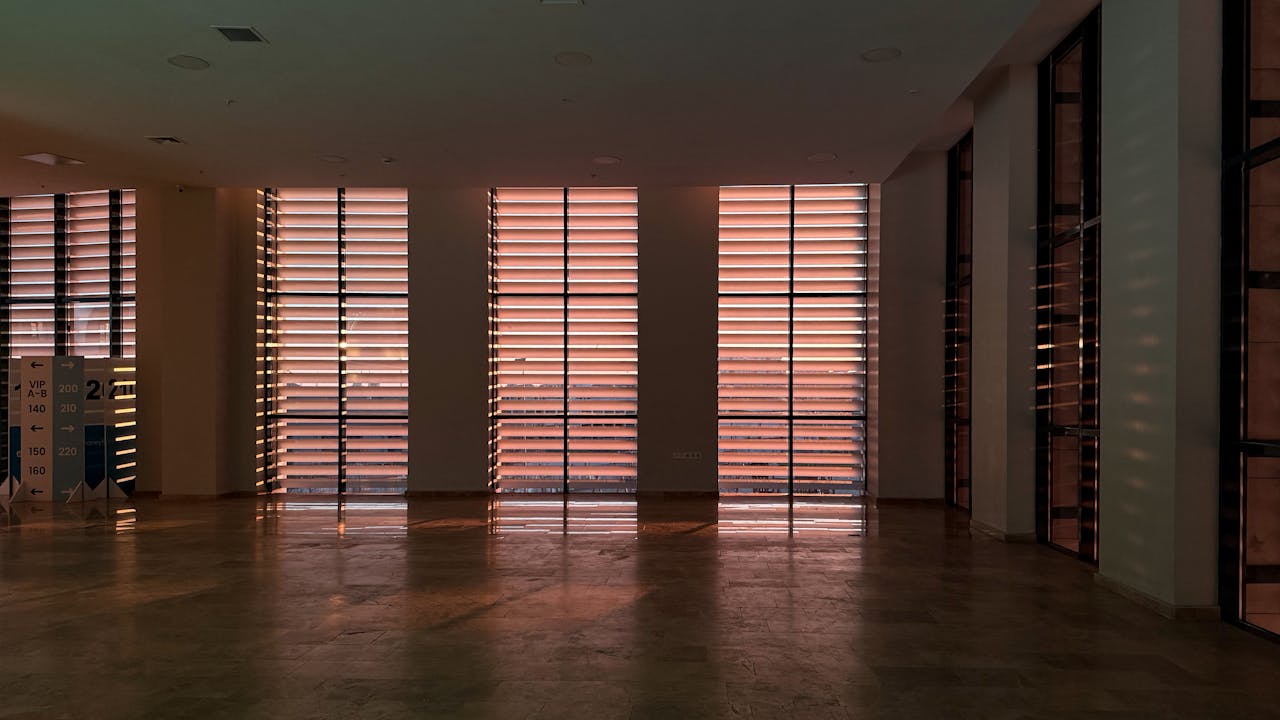 A spacious modern interior with sunlit louvered windows casting shadows.